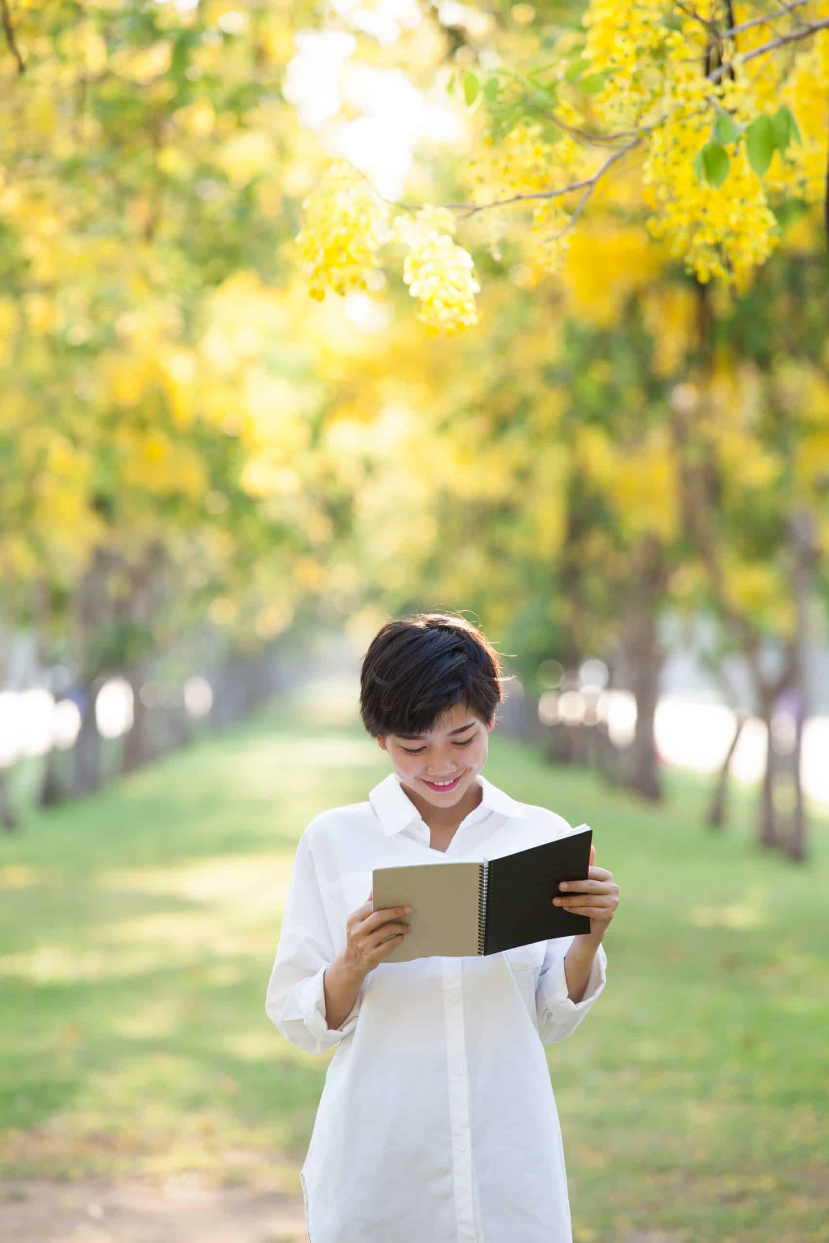 Stop frame/ Time Lapse Photography A young Asian man reading from a book from within a corridor of trees.