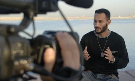 A man being filmed talking with the ocean as a backdrop.