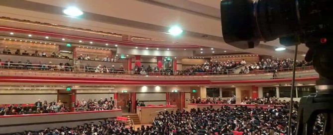 A very large conference in an old music hall. Attendees are already at their seats,