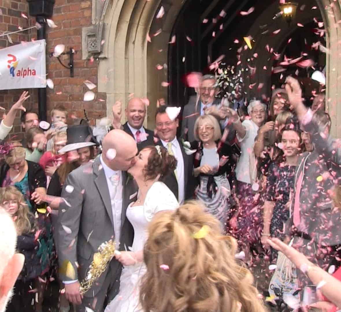 Live Stream Your Wedding A newly wedded couple leaving the church. Confetti is being thrown by the crowd that surrounds them.